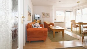 A living room with a sofa, a coffee table, and a TV. - Ostdeich Stübchen vacation apartment: Balcony & beach nearby (Büsum)