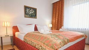 A hotel room with a bed, two bedside lamps, a painting, and a window with curtains. - Ostdeich Stübchen vacation apartment: Balcony & beach nearby (Büsum)