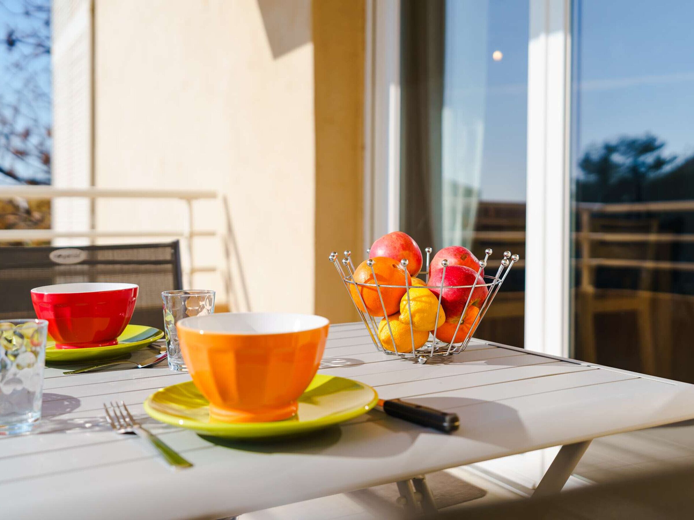 A dining table with a fruit basket, a red bowl, an orange bowl, and a green plate.