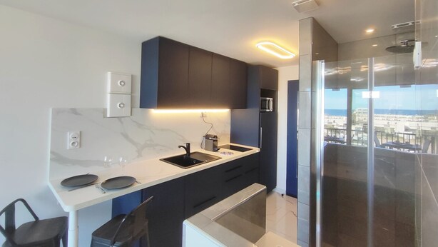 A modern kitchen with a built-in microwave, a sink, and a dining area with chairs. - Studio with AC, sea view - 2 guests (Le CAP D'AGDE)