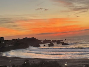 A coastal sunset with waves, rocky outcrops, and a distant shoreline. - Renovated studio, ocean view (Biarritz)