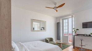 Ein Schlafzimmer mit Bett, Sessel, Schreibtisch, Fernseher und einem Balkon.