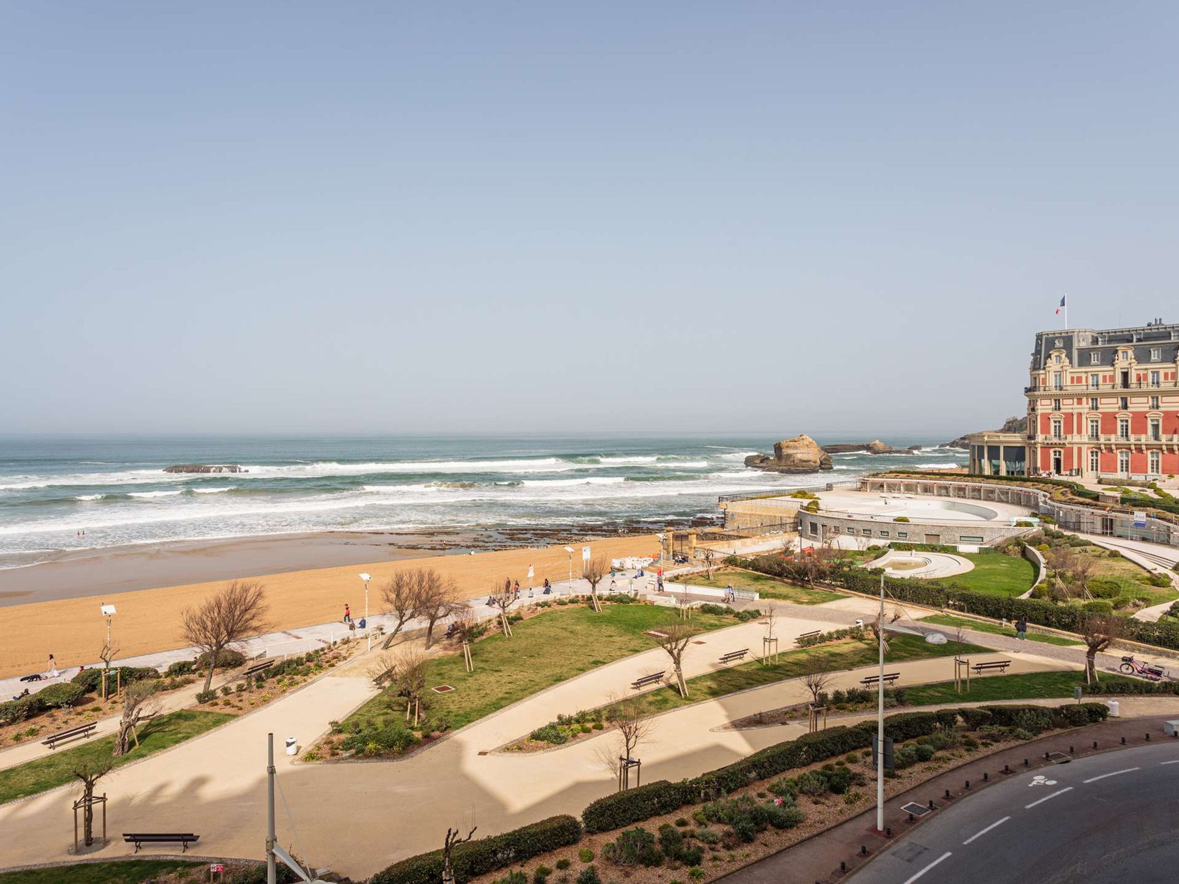 A coastal promenade with a beach, a circular plaza, and a large building with classical architecture.