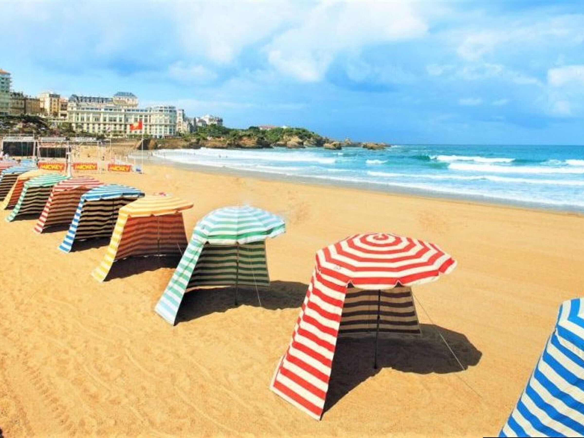 Une plage bordée de rangées de parasols rayés, avec un bâtiment en arrière-plan.