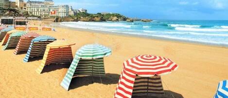Une plage bordée de rangées de parasols rayés, avec un bâtiment en arrière-plan.