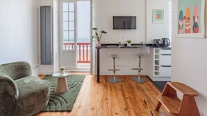 Eine moderne Wohnung mit Balkon, einer Küche inklusive Fernseher und einem Essbereich mit Barhocker.