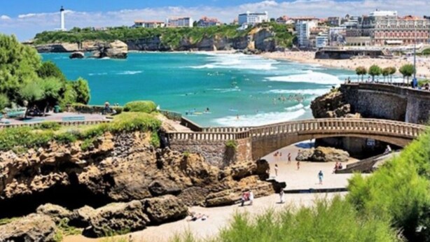 Eine Küstenansicht mit einer Brücke, felsigem Gelände und Gebäuden im Hintergrund.