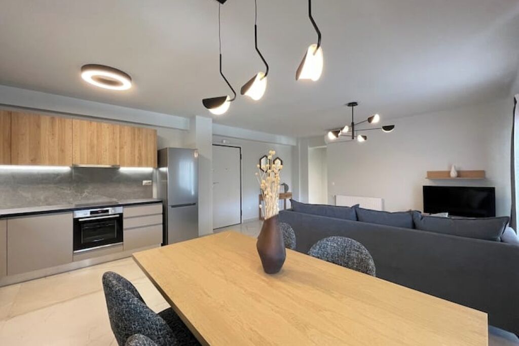 A modern kitchen with built-in appliances, a dining area with a wooden table and chairs, and a living area with a sofa and television.
