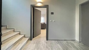 Ein Flur mit einer Treppe zu einem Wohnbereich, einer Tür mit der Aufschrift 'A1' und einer Leuchte darüber.
