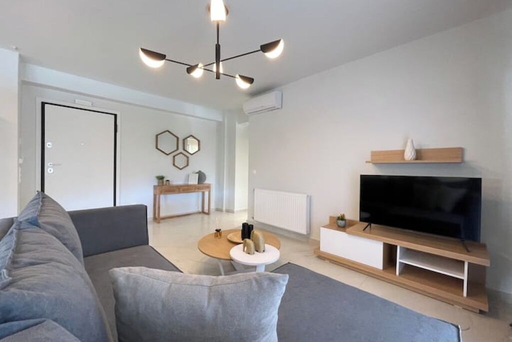 Una sala de estar moderna con un sofá, un televisor sobre un mueble de madera, una mesa de centro redonda y una lámpara en el techo.