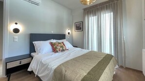 Ein Schlafzimmer mit einem Bett, Nachttischen, einer Klimaanlage, einer Pendelleuchte und einem Fenster mit Vorhängen.