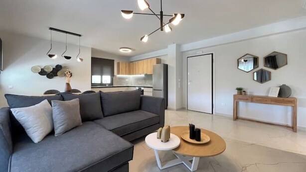 Ein modernes Wohnzimmer mit einem grauen Sofa, einem runden Couchtisch und einer Küche im Hintergrund.