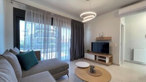 Una sala de estar moderna con un sofá, una mesa de centro redonda, un televisor sobre un mueble bajo y una ventana con cortinas.