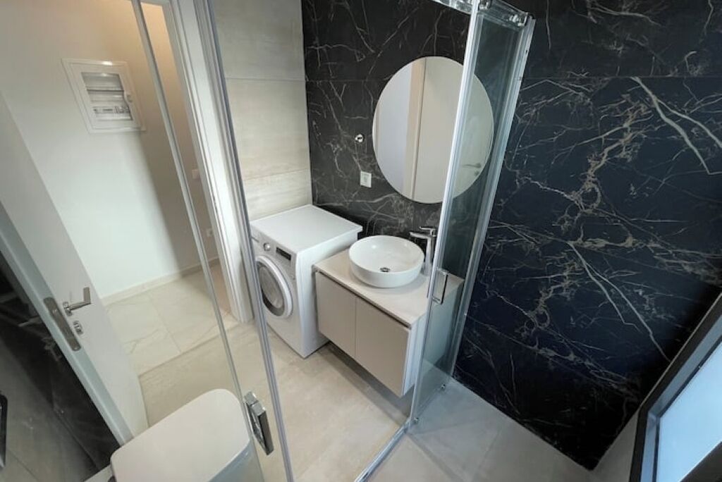 A modern bathroom with a washing machine, a sink, and a glass shower enclosure.