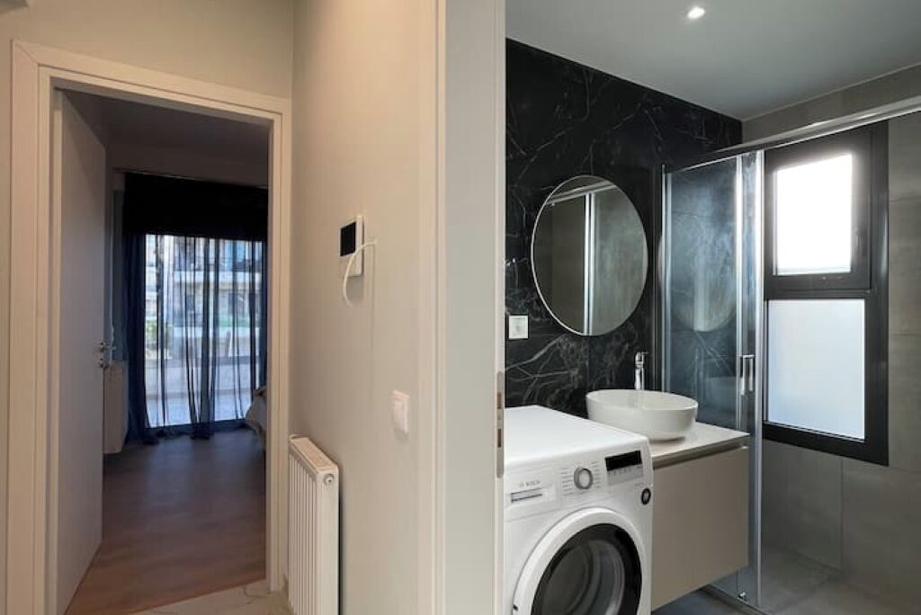 A modern bathroom with a washing machine, a sink, and a glass shower enclosure.