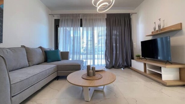 Una sala de estar moderna con un sofá, una mesa redonda de centro, un televisor de pantalla plana y una lámpara colgante.
