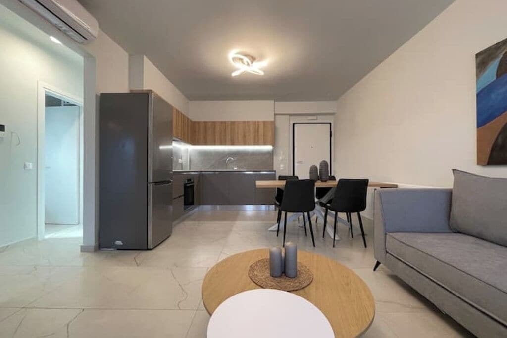 A modern living room with a grey sofa, a round coffee table, and a dining area with a wooden table and chairs.