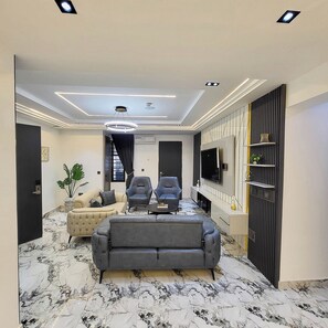 Un salon moderne comprenant un canapé, deux fauteuils, un téléviseur et un panneau décoratif mural.