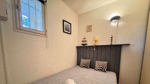 A bedroom with a bed, pillows, a window, a wall-mounted shelf with decorative items, and a wall-mounted lamp. - Apartment with lake view - 4 guests (Six-Fours-les-Plages)