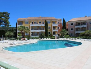 Une piscine entourée de chaises longues, elle-même bordée d’immeubles à plusieurs étages dotés de balcons.