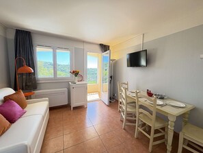Un espace de vie compact comprenant un coin repas, un canapé, un téléviseur et une fenêtre donnant sur un beau paysage.