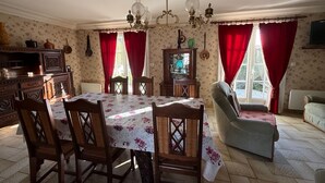 Ein Essbereich mit einem Tisch für vier Personen, umgeben von Stühlen, einer Chandelüster und einer Couch.