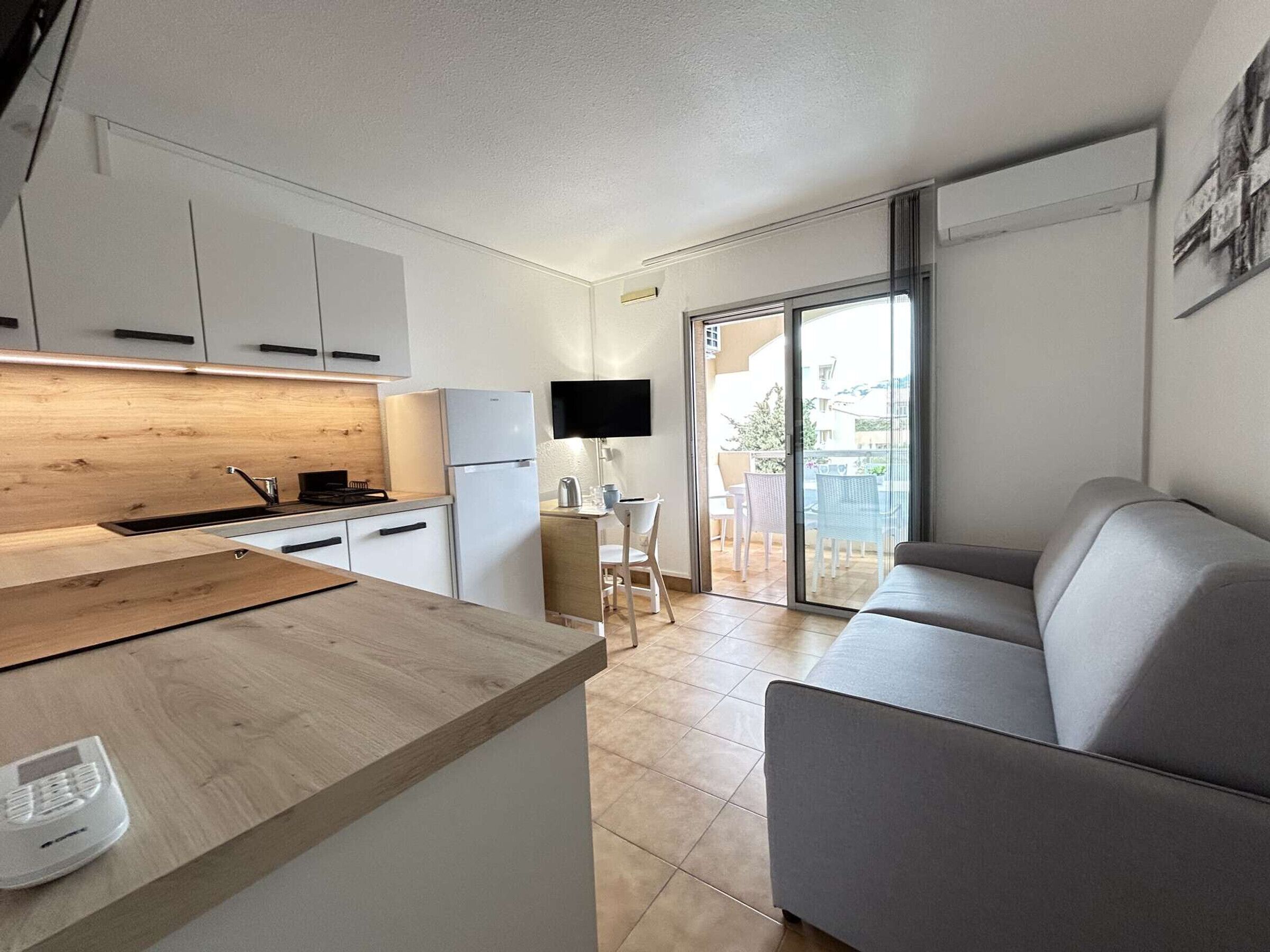A compact kitchen with a wooden countertop, a built-in stove, and a refrigerator. There is a dining area with a table and chairs, and a sliding glass door leading to an outdoor patio.