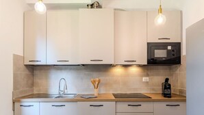 Une cuisine moderne avec des meubles blancs, un évier en acier inoxydable, un four à micro-ondes et des ustensiles en bois posés sur le plan de travail.