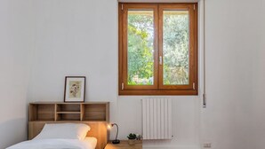 Une chambre à coucher comprenant un lit, une table de chevet, une lampe, un radiateur et une fenêtre donnant sur un paysage verdoyant.