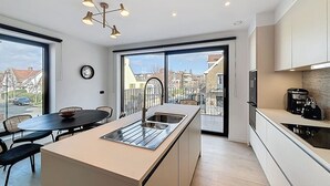 A modern kitchen with a central island, large windows, and a dining area. - Flat Seadune - De Panne (De Panne)