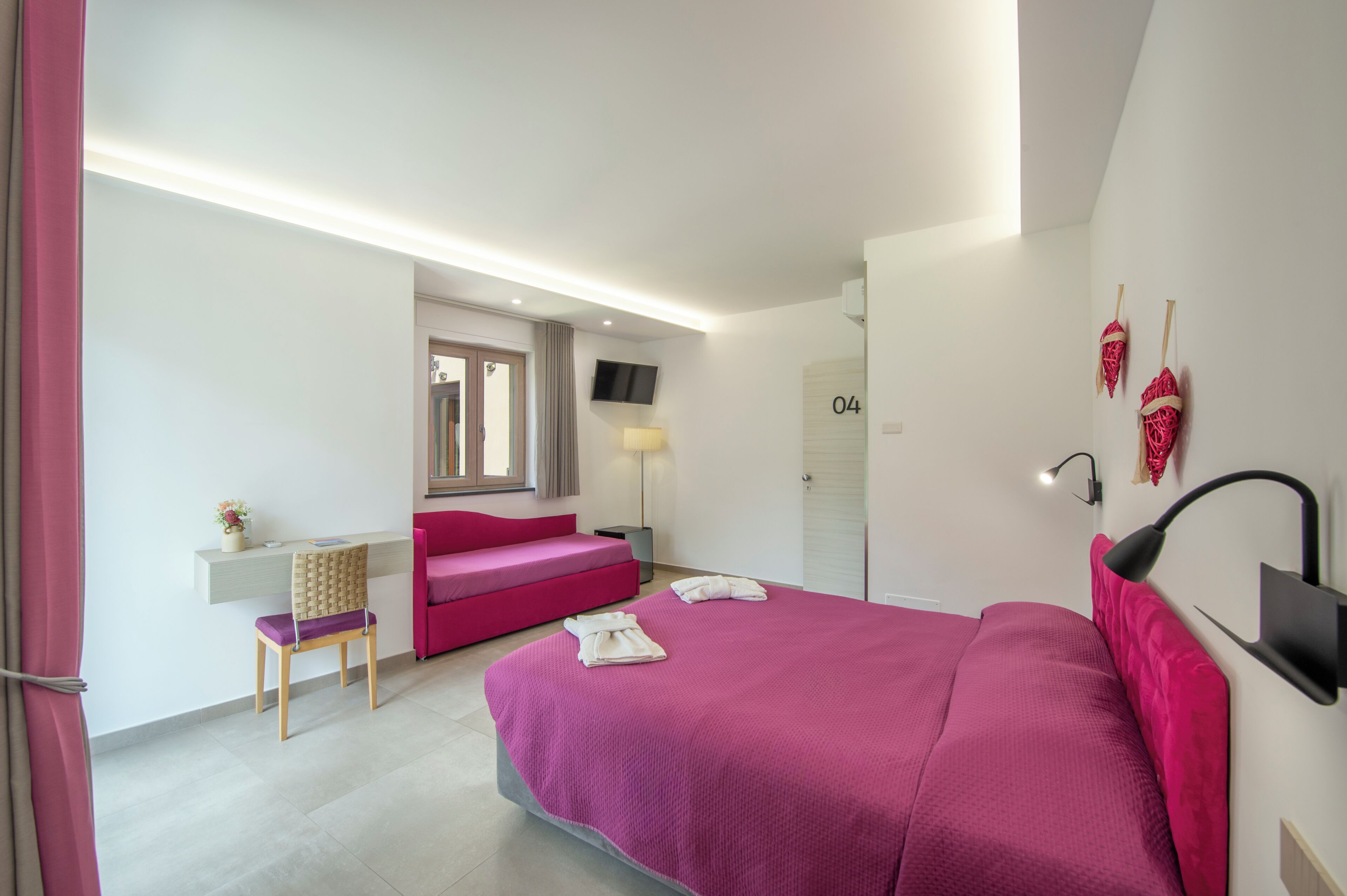 Un dormitorio moderno con una cama grande, un escritorio, una silla, un sofá, un televisor y una lámpara.