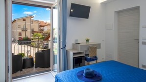 Hotelkamer met een bed, bureau, stoel, televisie en balkon met zitgelegenheid.