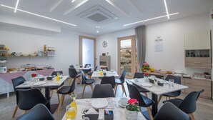 Een moderne eetruimte met meerdere tafels en stoelen, een keuken met inbouwapparatuur, en uitzicht door de deur.