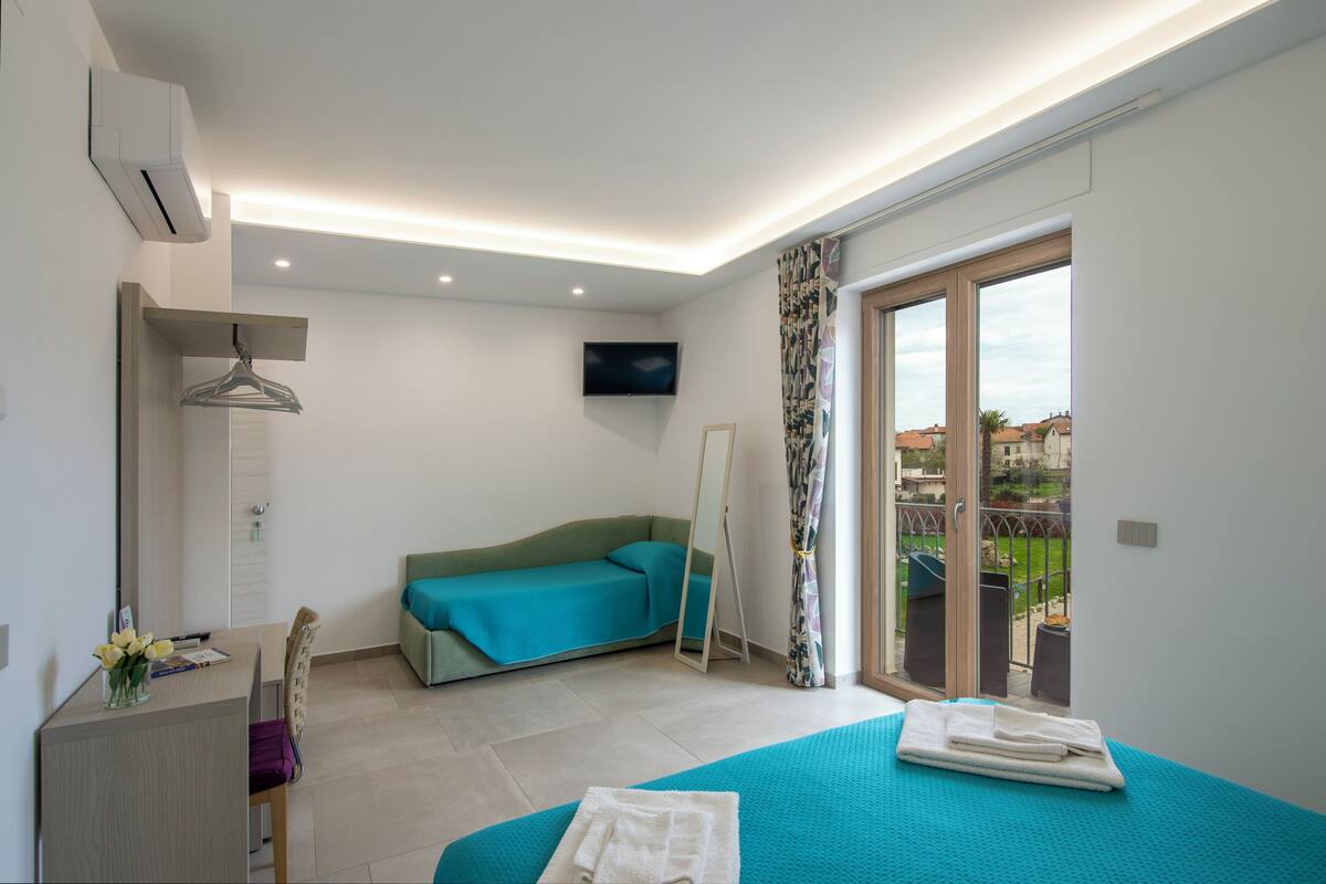 Habitació d'hotel moderna amb llit, escriptori, sofà, televisió i un balcó amb vistes.