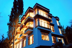 Un edificio de varios pisos con balcones y ventanas amplias, rodeado de árboles.