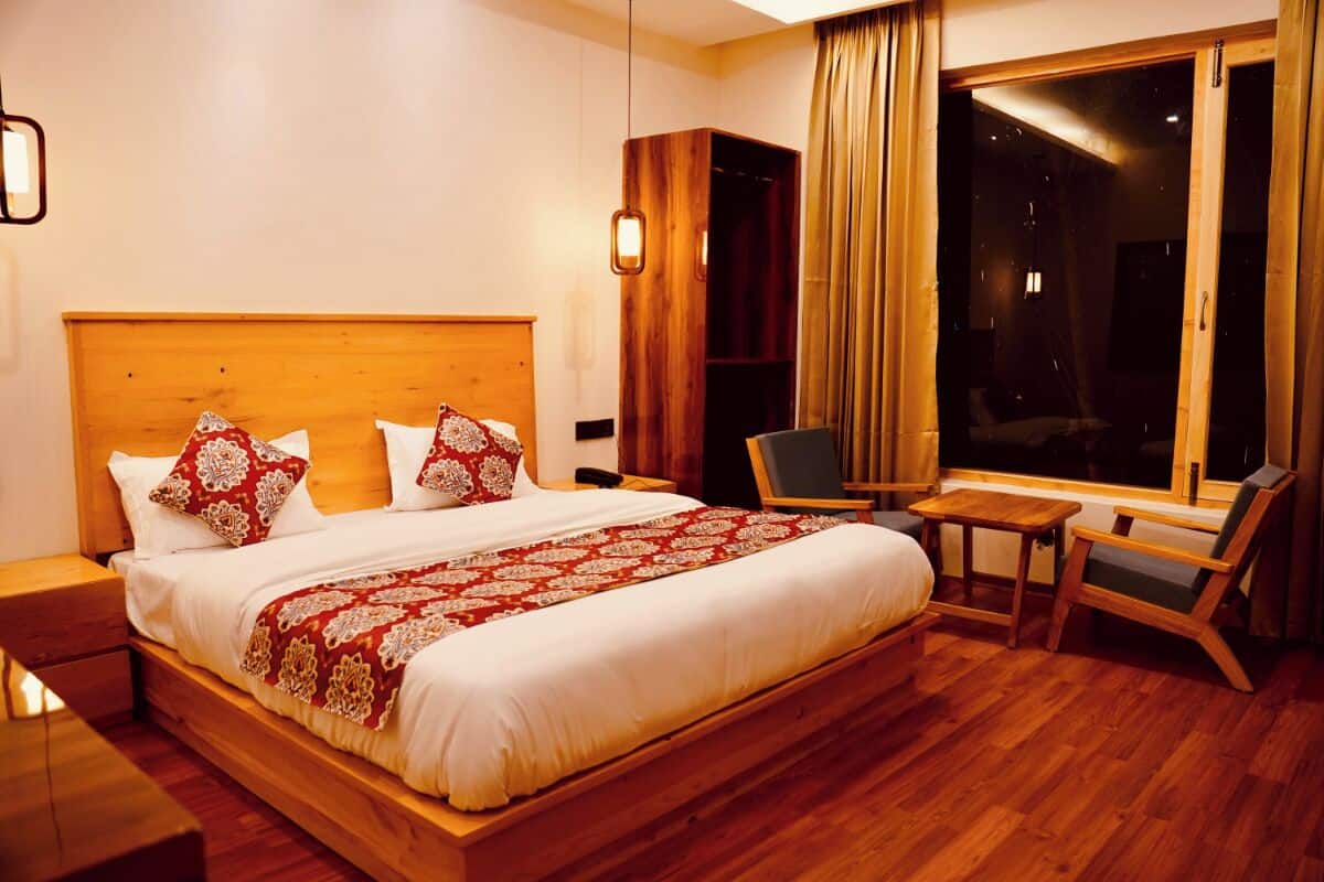 A hotel room with a wooden bed, a small table, a chair, a wardrobe, and a large window.