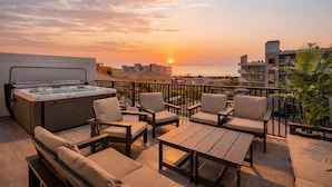 Une terrasse sur le toit avec un jacuzzi, un espace salon et une vue sur le coucher de soleil sur l’océan.