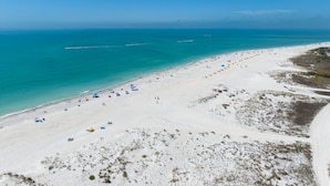 Une plage de sable blanc, avec une eau turquoise et limpide, et quelques parasols.