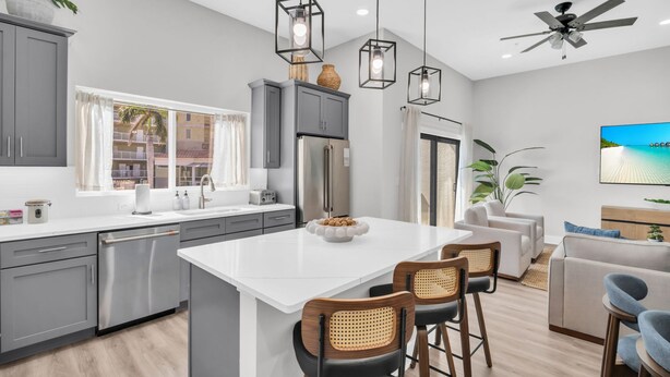 Une cuisine moderne avec des meubles gris, un îlot central blanc et des luminaires suspendus.