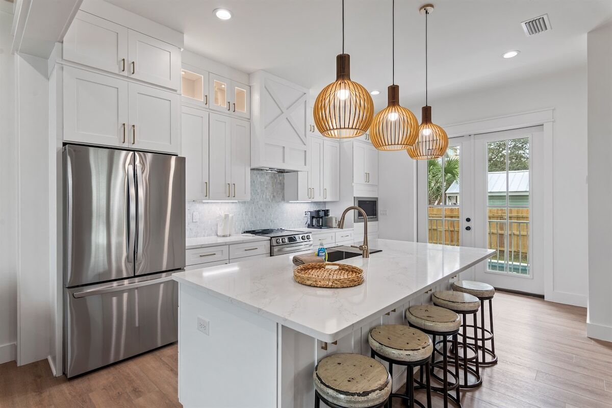 A modern kitchen with white cabinetry, stainless steel appliances, a large island with stools, and pendant lighting.