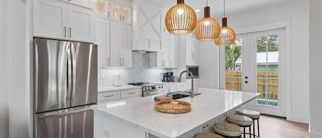 A modern kitchen with white cabinetry, stainless steel appliances, a large island with stools, and pendant lighting.