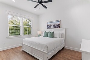 Ein Schlafzimmer mit einem Bett, einem Deckenventilator, einem Fenster mit Jalousien und einem Bild an der Wand.