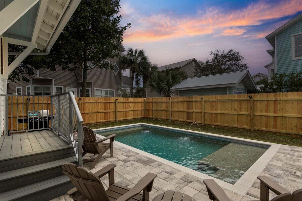 A backyard with a swimming pool, wooden deck, and outdoor furniture.