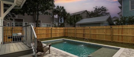 Un patio trasero con piscina, terraza de madera y mobiliario exterior.