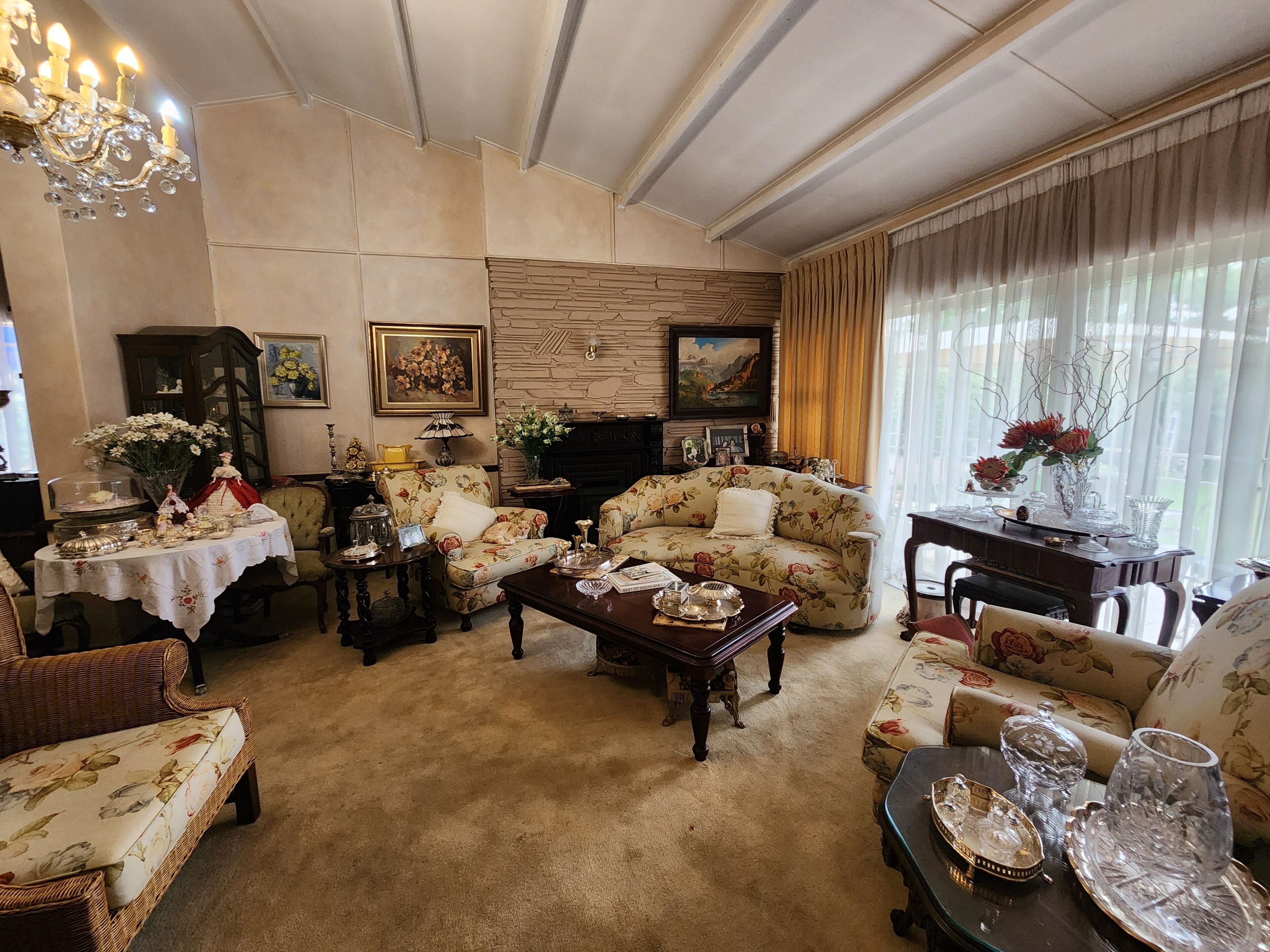 A cozy living room with a fireplace, floral-patterned sofas, a coffee table, and a chandelier.