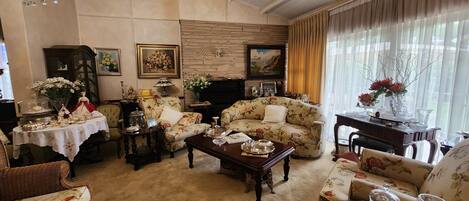 A cozy living room with a fireplace, floral-patterned sofas, a coffee table, and a chandelier.