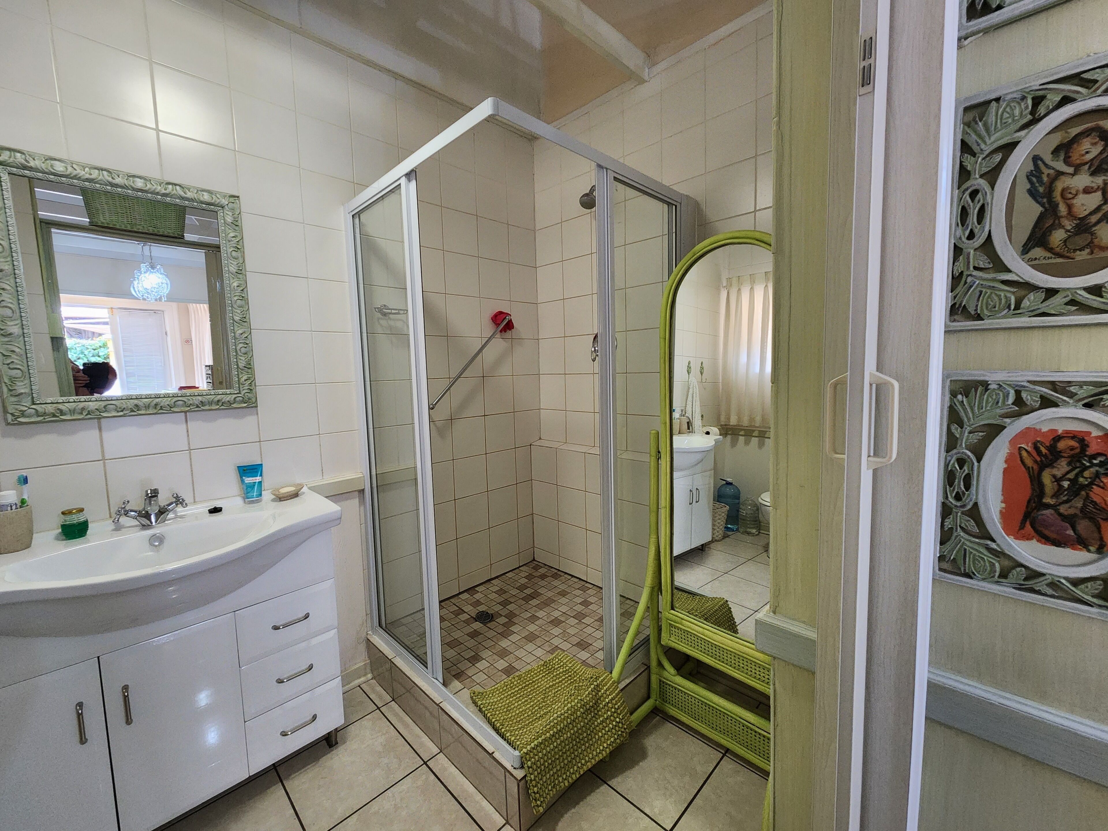 A bathroom with a glass-enclosed shower, a sink with a mirror, and a decorative wall panel.