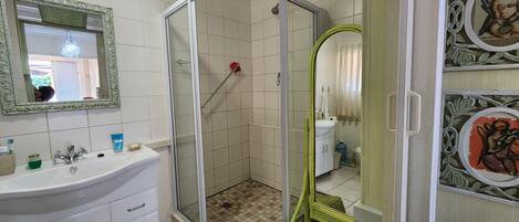 A bathroom with a glass-enclosed shower, a sink with a mirror, and a decorative wall panel.