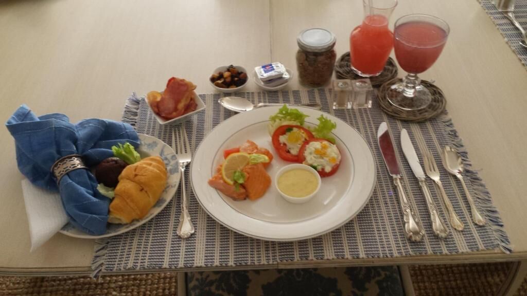 Ett bord med en tallrik mat, en servett, ett glas med röd dryck och en burk med sylt.