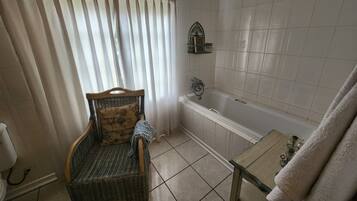 Un baño con bañera, una silla, una mesita y una toalla.